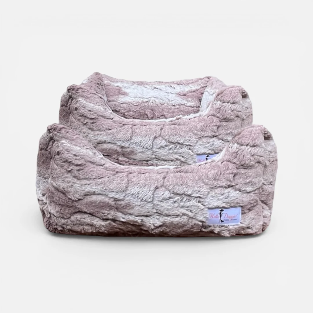 Soft plush dog bed in pale pink/gray faux fur with a small label tag on the corner, cozy and inviting.