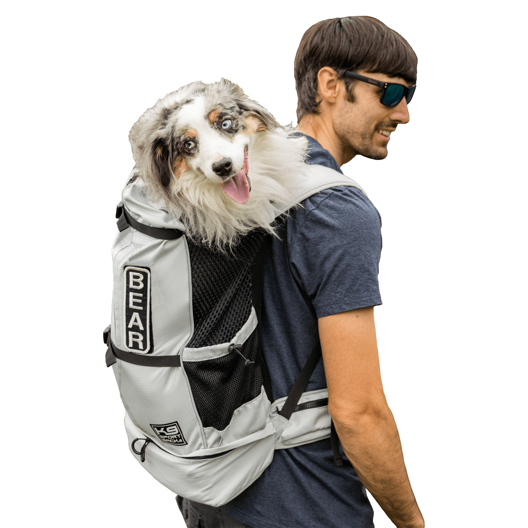 Man wearing a dark t-shirt and sunglasses carries a fluffy white and gray dog in a front-facing backpack carrier.